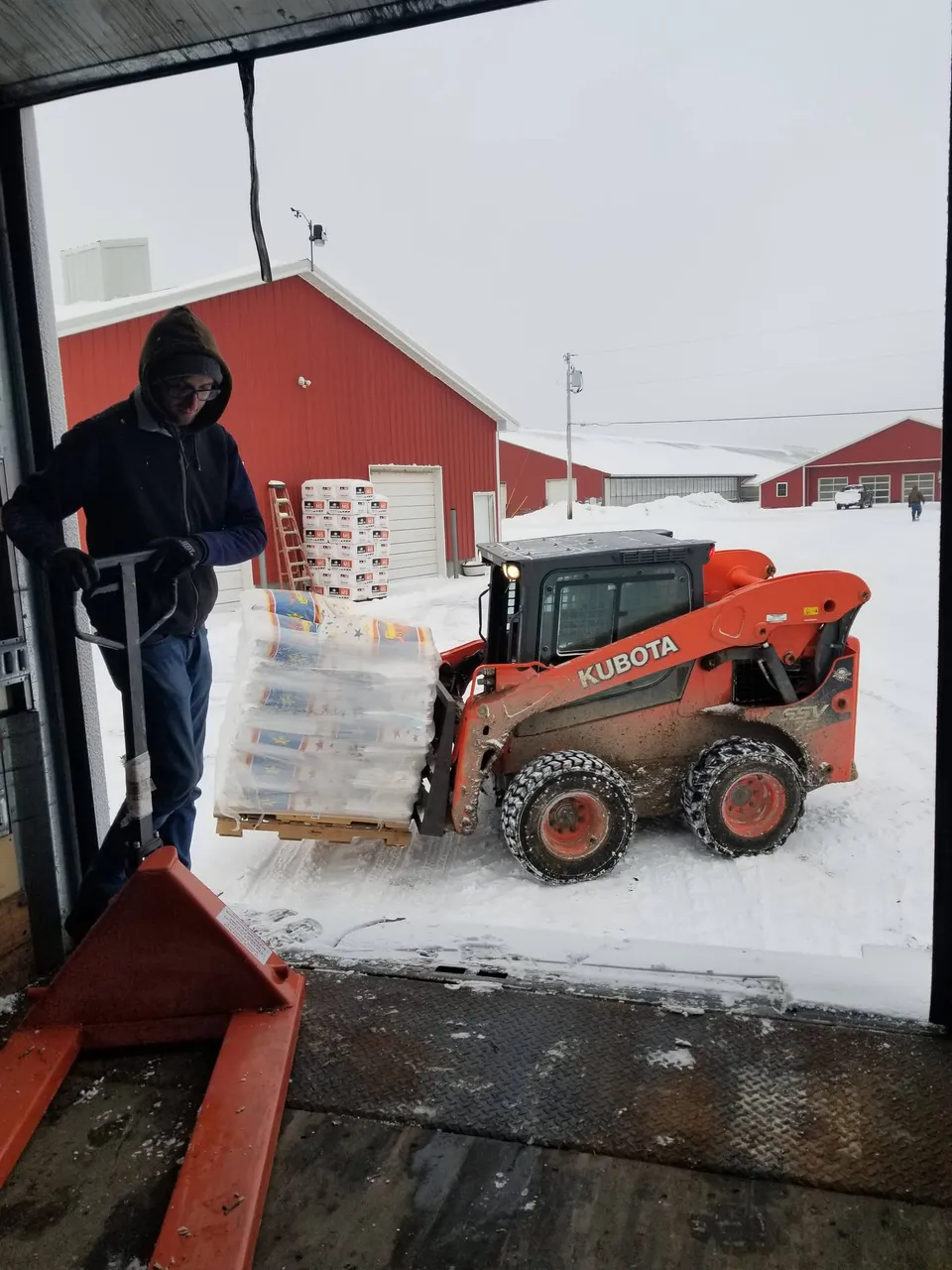 Loading feed bags with a Kubota in front of red barns on a snowy day